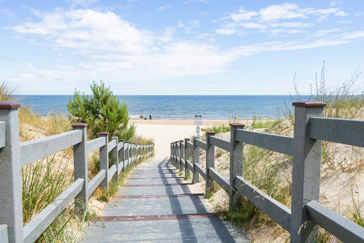 A flat staircase with wooden railings leads through sand dunes to the sea.