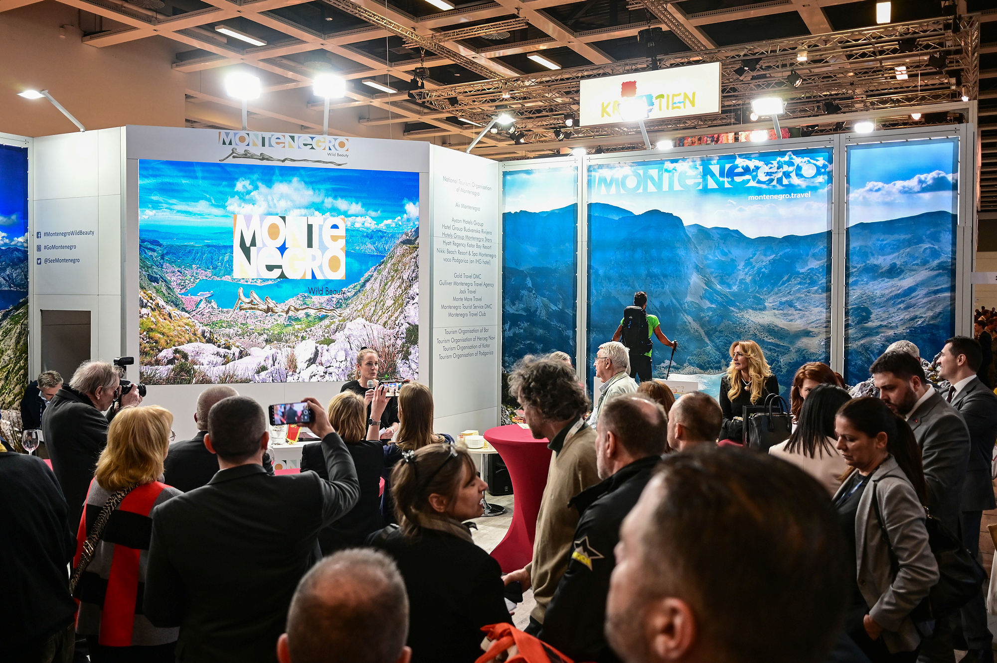 Groups of people with their backs to the camera in the foreground, an exhibitor’s stand with images of landscapes, including mountain scenery in Montenegro, in the background.
