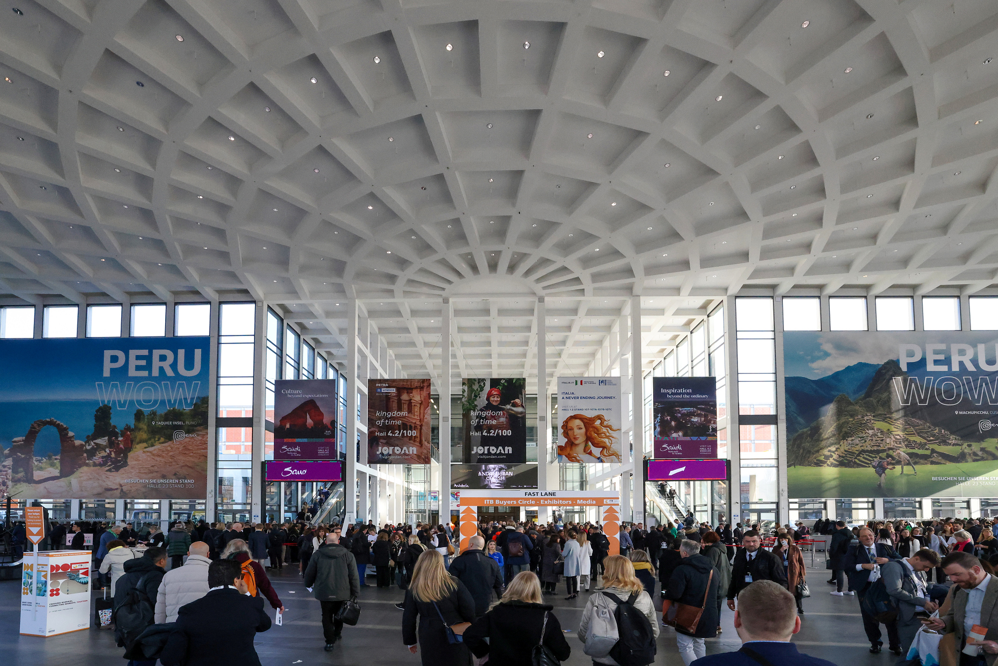 People in the South Entrance of ITB Berlin, promotional posters in the background. 