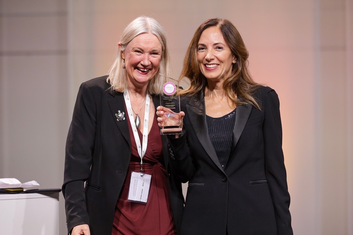 Two women smiling into the camera and holding an award. 