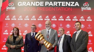 Albanian representatives in front of a Giro d'Italia press wall. The trophy of the event is in the centre. 