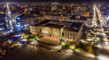 Long shot of the illuminated Tirana Biennial by night.