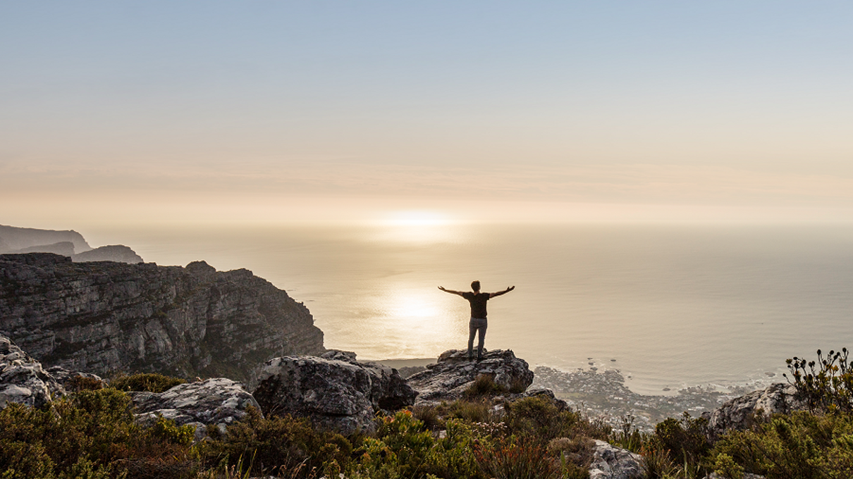 A person on a mountain, with the sea and the horizon in the background.