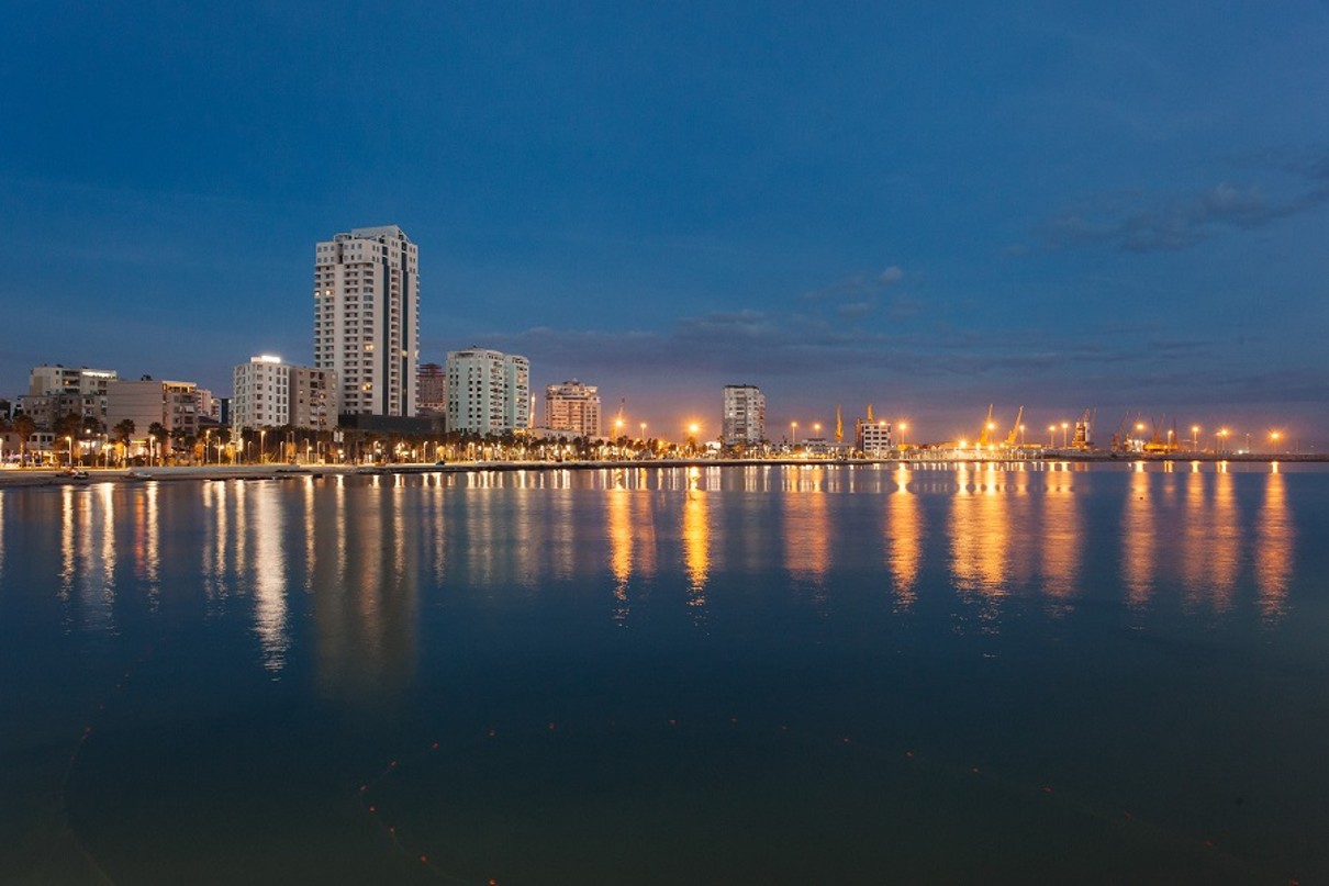 Skyscrapers in the background, water in the foreground, reflecting the light of the city.