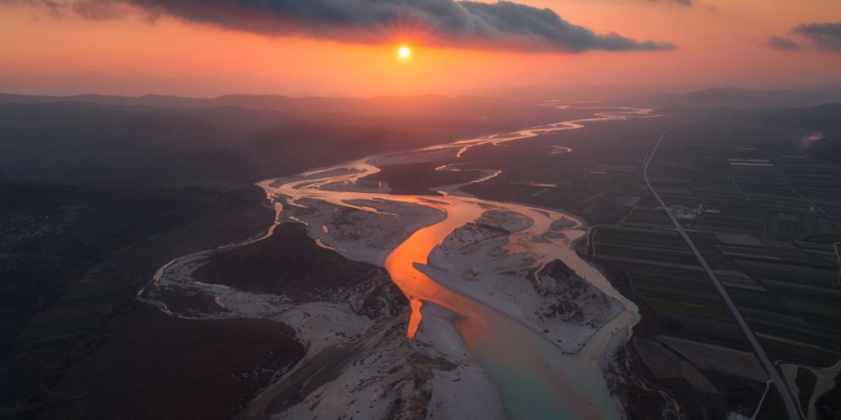 Ein Fluss mit einem Sonnenuntergang im Hintergrund, der Himmel ist rot.