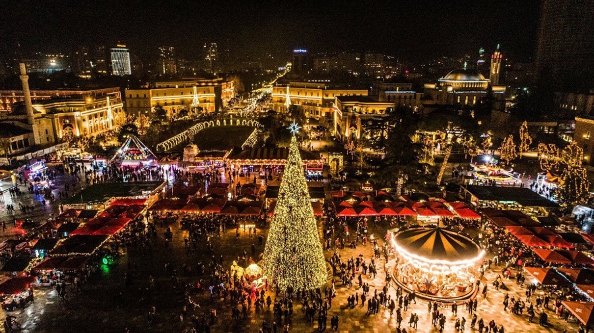 Ein Weihnachtsmarkt mit Lichtern und einem Weihnachtsbaum und Karussell in der Mitte des Bildes. 