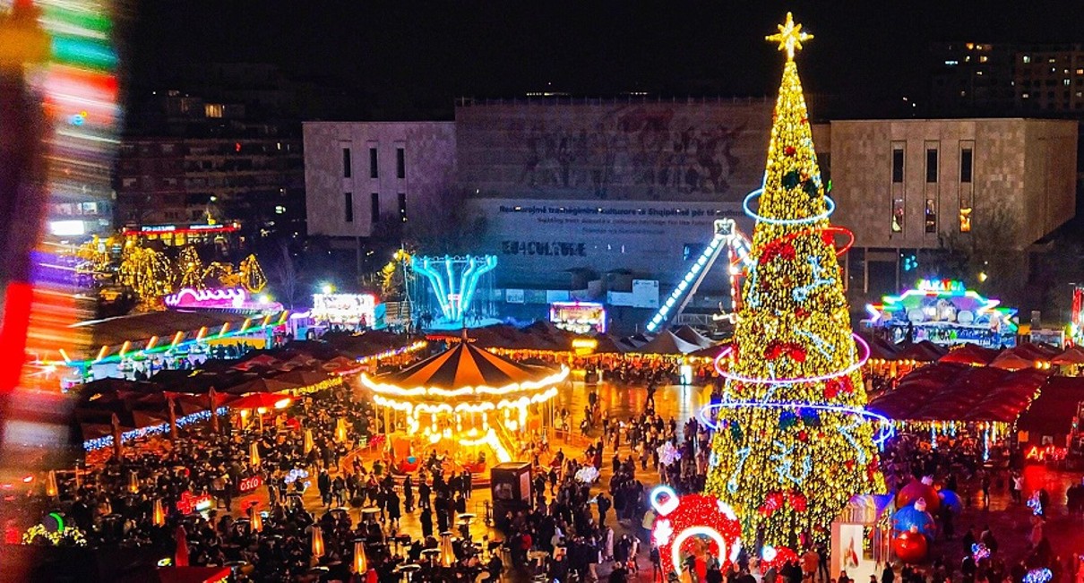 Ein bunter Weihnachtsmarkt mit vielen Menschen, einem Weihnachtsbaum und einem Karussell.