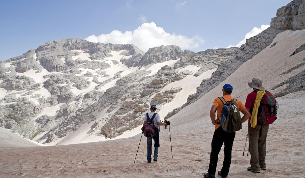 Three people hiking on the summit of a mountain, snow-covered mountains in the background. 