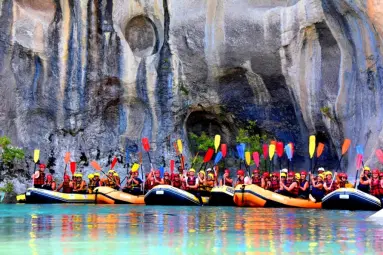 Eine Gruppe von Menschen in Booten auf dem Wasser, die ihre Paddel hochhalten. 