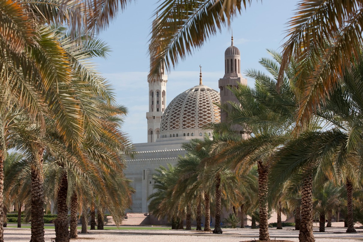 Die Sultan Qaboos Moschee in Maskat im Hintergrund und Palmen im Vordergrund.